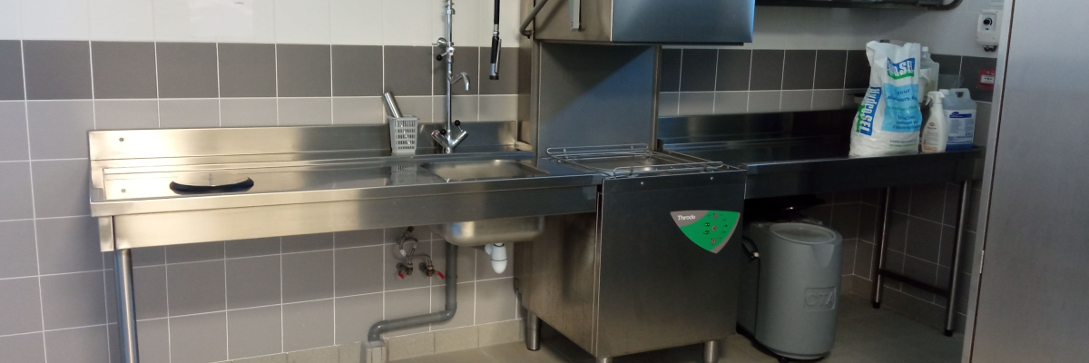 Cuisine avec plan de travail, lave-vaisselle, évier, robinet à bras articulé, poubelle et produits de nettoyage.