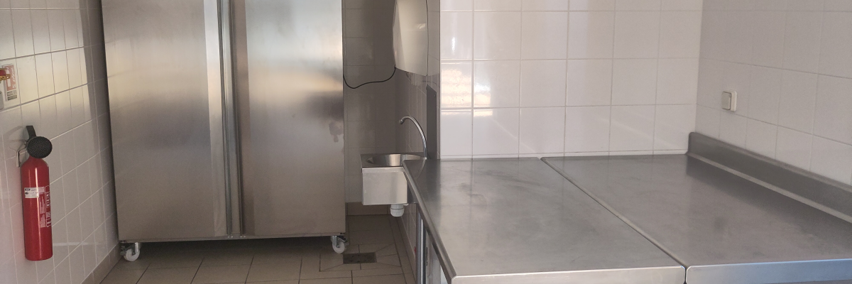 Cuisine avec réfrigérateur, évier, table en acier inoxydable et extincteur.