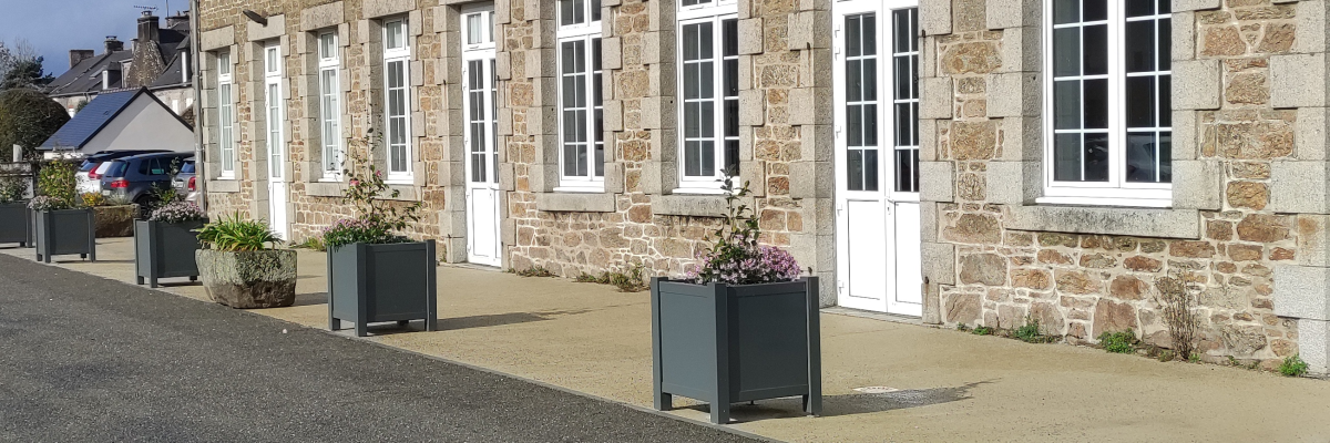 Bâtiment en pierre avec plusieurs fenêtres, porte d'entrée, poubelle et plantes en pot.