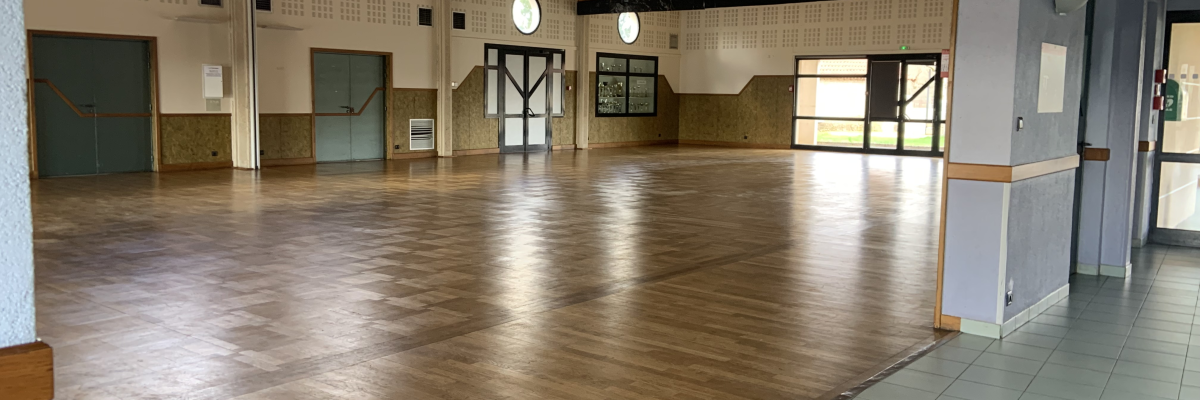 Salle spacieuse avec parquet, murs beiges, fenêtres, portes et sol carrelé.