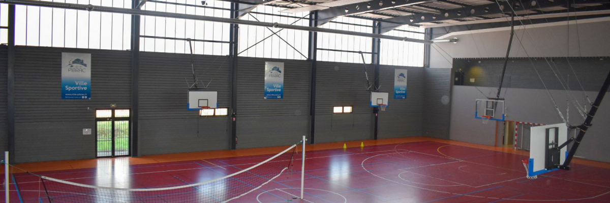 Salle de sport avec paniers de basket, filets de volley-ball et lignes de terrain.