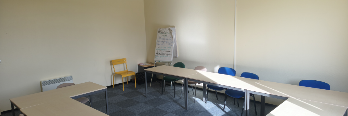 Salle de réunion avec tables, chaises, flipchart, climatiseur et rideaux.
