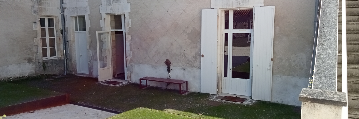 Bâtiment avec portes ouvertes, banc, pelouse et allée en béton.