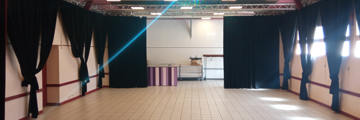 Salle avec projecteur, rideaux, sol en bois et carrelage, éclairage suspendu.