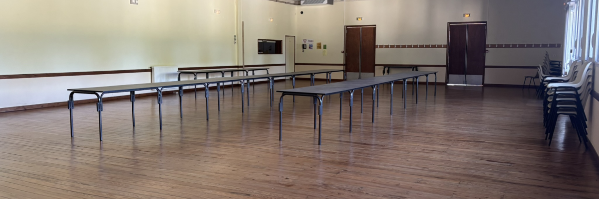 Salle avec plancher en bois, tables, chaises, portes et murs beiges.