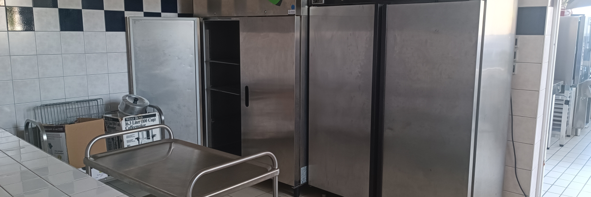 Salle avec chariot, deux grands réfrigérateurs, panier et porte.