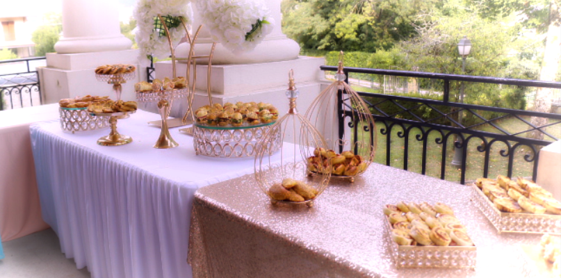 Table avec nappes, plateaux de nourriture, fleurs et vue sur jardin.