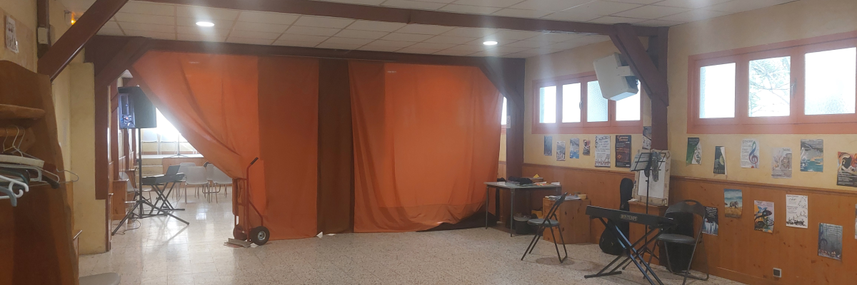 Salle vide avec tréteaux, rideau, tables, chaises et panneaux d'affichage.