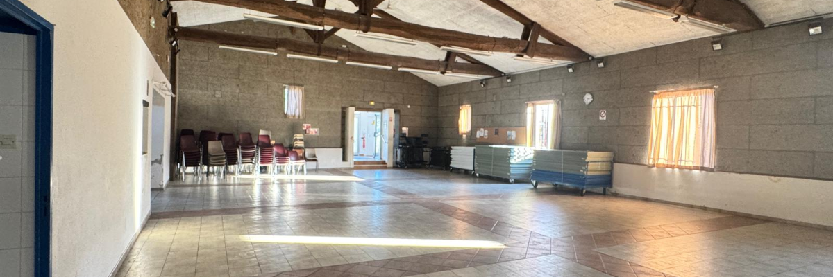 Salle avec tables, chaises, canapé et poufs. Poutre métallique, fenêtres et portes.