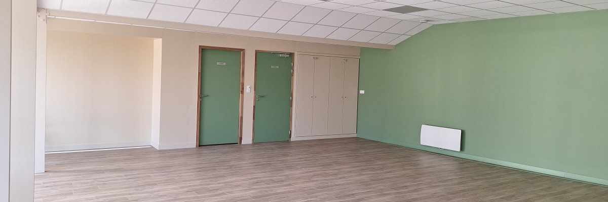 Salle vide avec portes vertes, radiateur et plafond à dalles.
