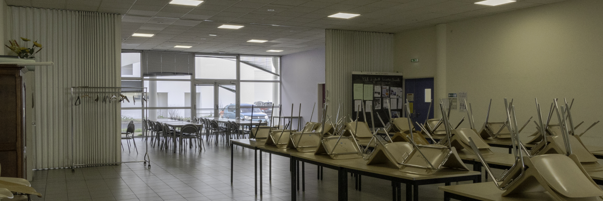 Salle avec tables, chaises, rideaux, et porte-manteaux.