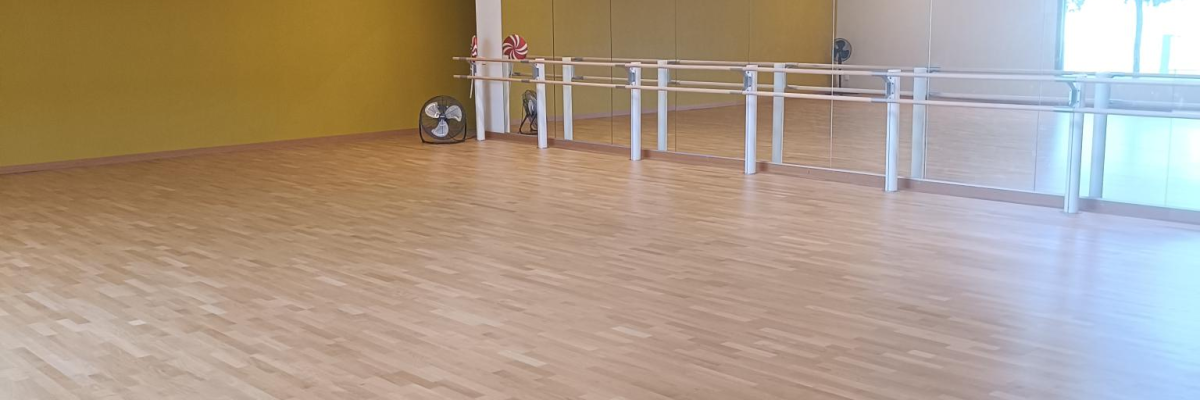 Salle avec parquet, barres de ballet, éclairage et murs jaunes.