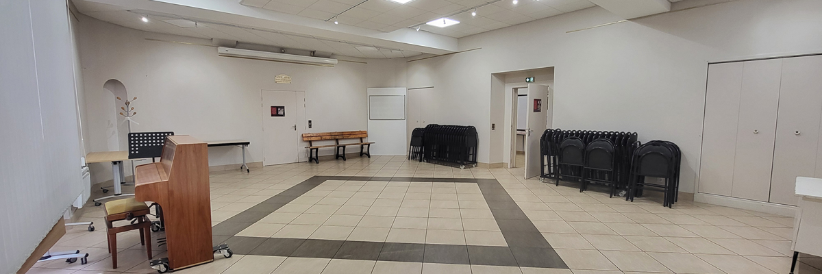 Salle avec piano, pupitre, tables, chaises, tableau blanc et porte.