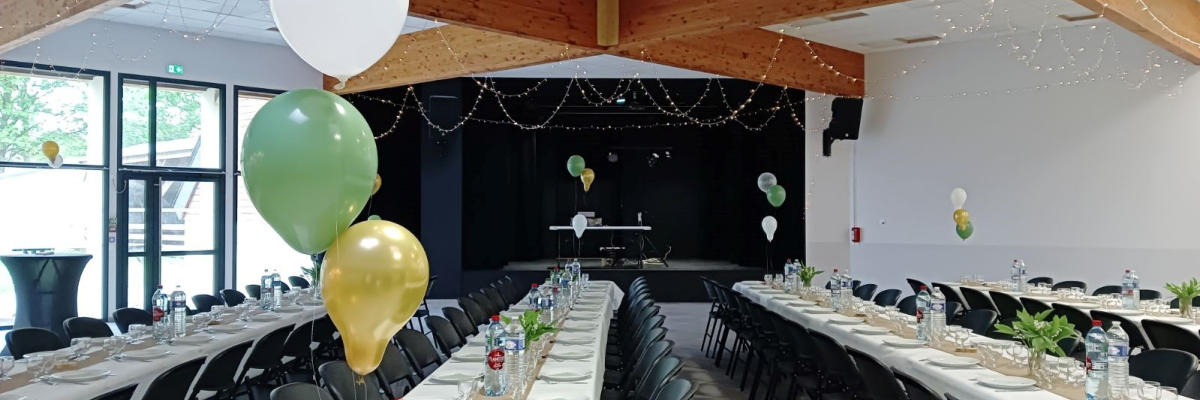 Salle avec tables, chaises, ballons, vaisselle, et guirlandes.