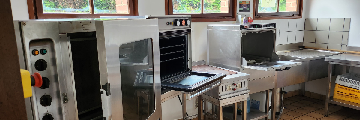 Cuisine équipée avec fours, table de travail, étagères et éviers.