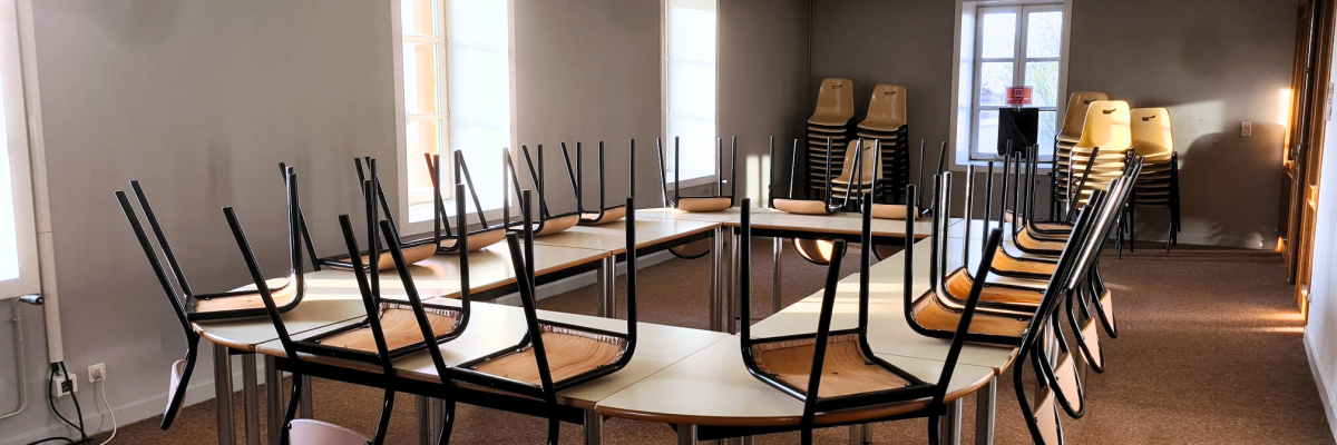 Salle avec tables, chaises, vidéo projecteur, rideaux.