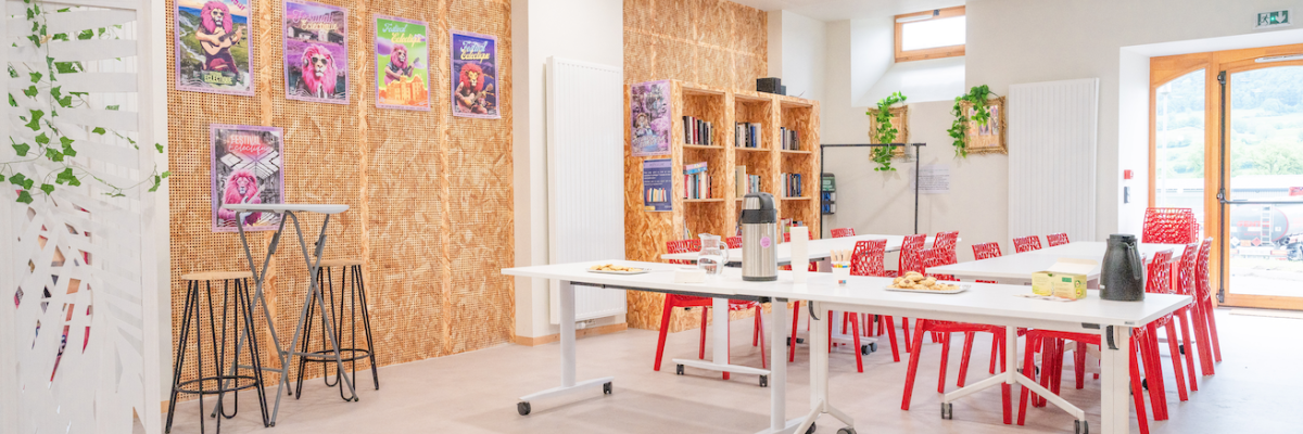 Salle avec tables, chaises, étagères, tableaux, affiches et plantes.