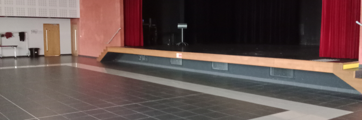 Salle avec sol en damier noir et blanc, scène avec rideaux rouges, éclairages suspendus, et porte blanche.