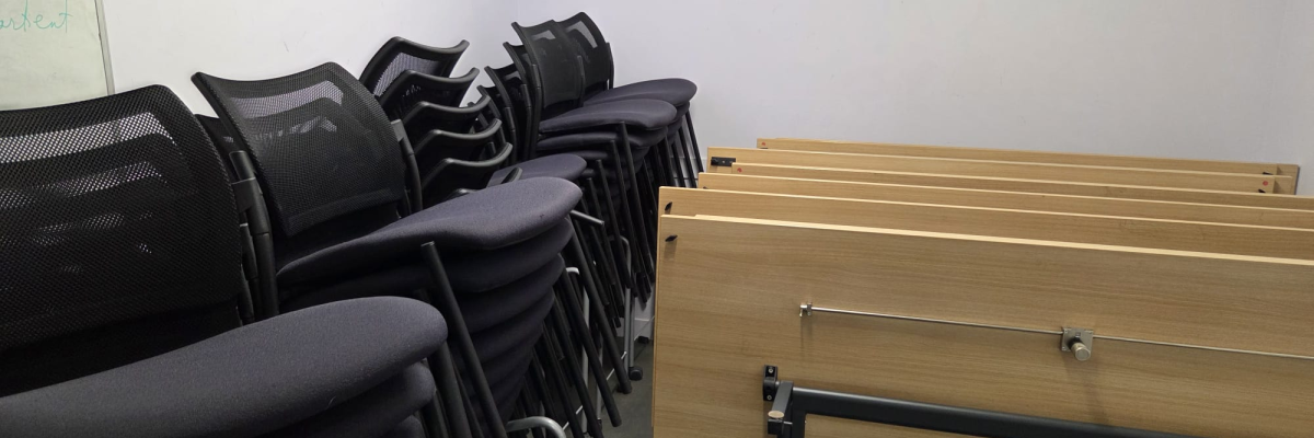 Salle de classe avec rangées de pupitres et chaises. Tableau blanc à gauche.