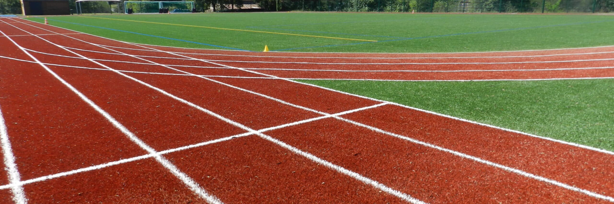 Piste d'athlétisme avec herbe, lignes, et ciel.