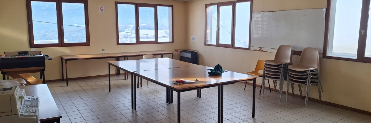 Salle avec tables, chaises, tableau blanc, fenêtres et équipement informatique.