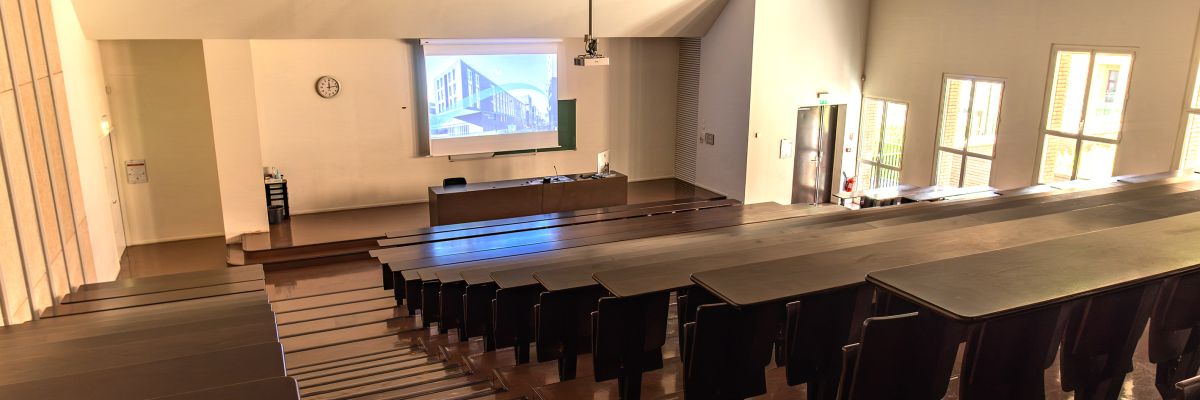 Salle de classe avec tables, chaises, écran, projecteur et horloge.