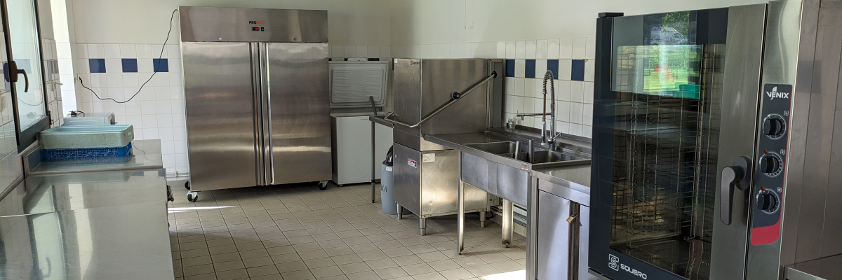 Cuisine professionnelle avec plan de travail, frigo, évier, four et hotte.