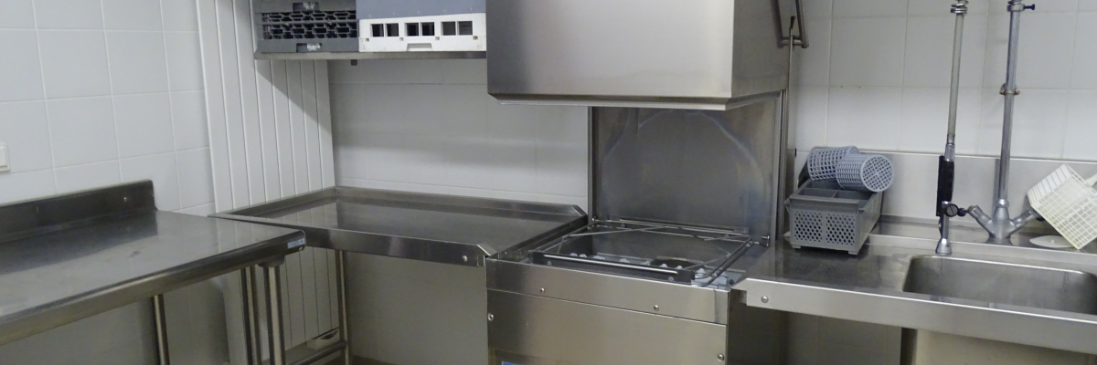 Cuisine avec lave-vaisselle industriel, étagères, plan de travail, tuyau d'arrosage et éviers.