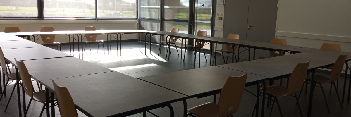 Salle avec tables en L, chaises et portes vitrées.