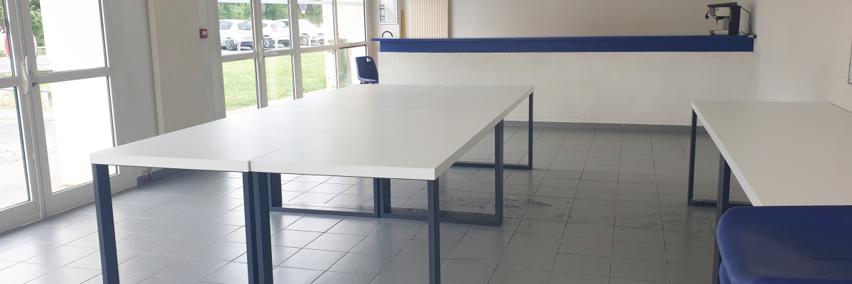 Salle avec tables, chaises, tableau blanc, vidéo projecteur et porte.