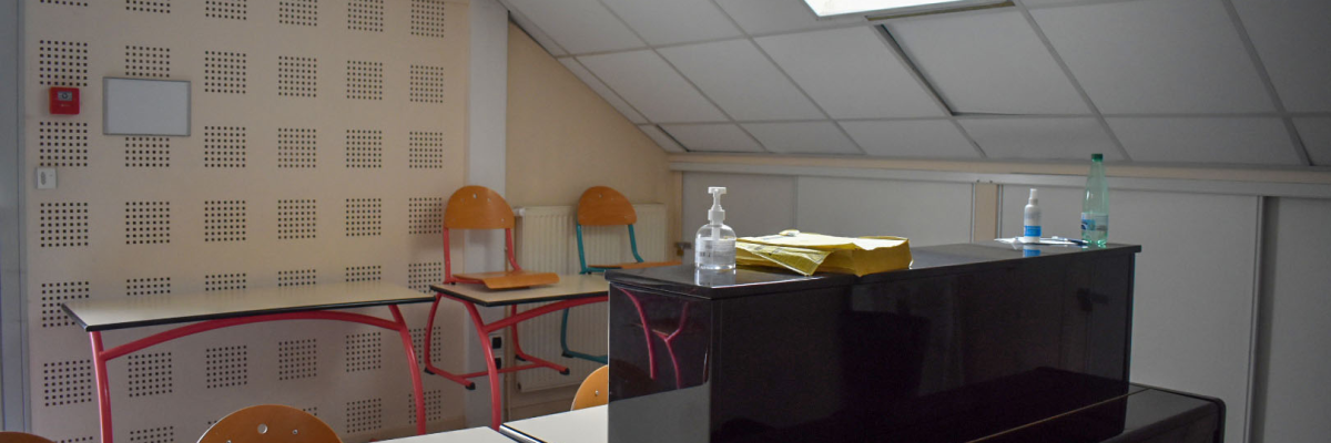Salle de classe avec tables, chaises, bouteilles d'eau, documents et tableau blanc.