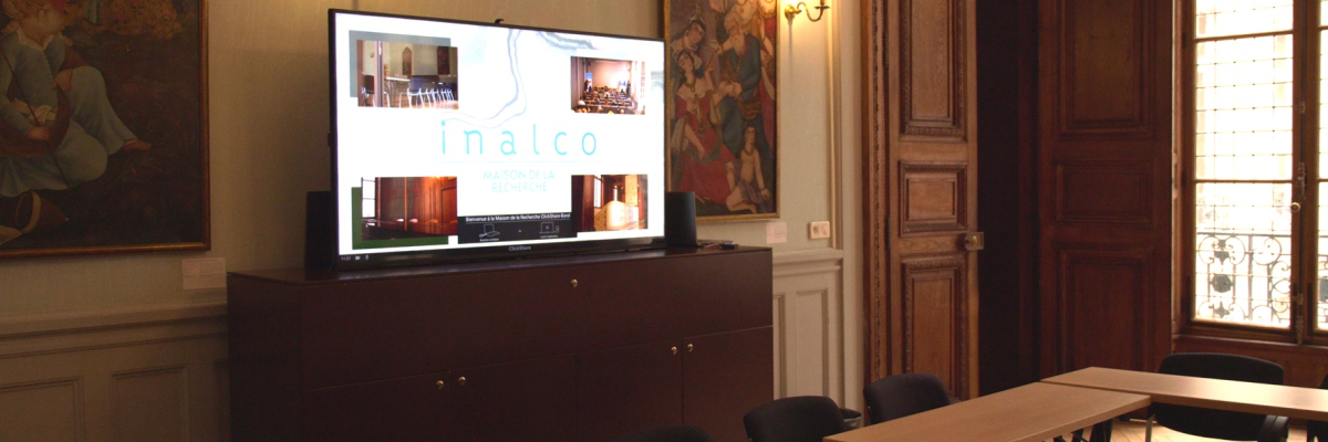 Salle avec tables, chaises, écran, meubles et peintures murales.