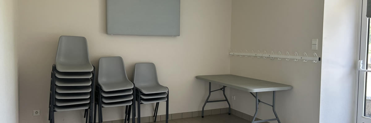 Salle avec table, chaises empilées, tableau et porte-manteau.
