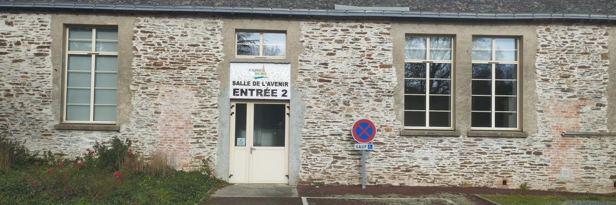 Bâtiment en pierre avec entrée marquée "Salle de l'Entente Entrée 2", parking avec places handicapées, panneau d'interdiction de tourner à gauche.