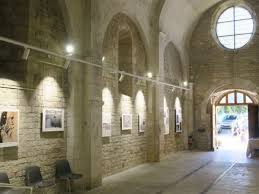 Salle d'exposition avec cadres, bancs, lumières et arches.