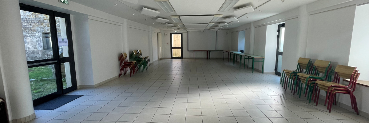 Salle vide avec portes, chaises, plantes et lumières au plafond.