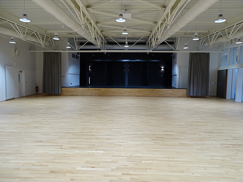 Salle vide avec sol en bois, plafond métallique et rideaux noirs.