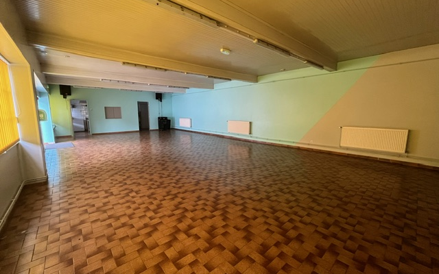 Salle vide avec parquet, murs peints, radiateurs et porte.
