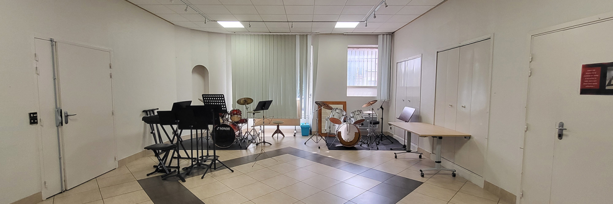 Salle avec batterie, piano, pupitres, tables et chaises.