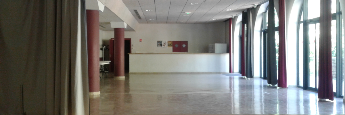 Salle avec plancher en bois, colonnes rouges, fenêtres, rideaux, et éclairage au plafond.