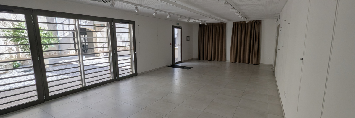 Salle vide avec grandes fenêtres, portes, stores, éclairage encastré et placards.