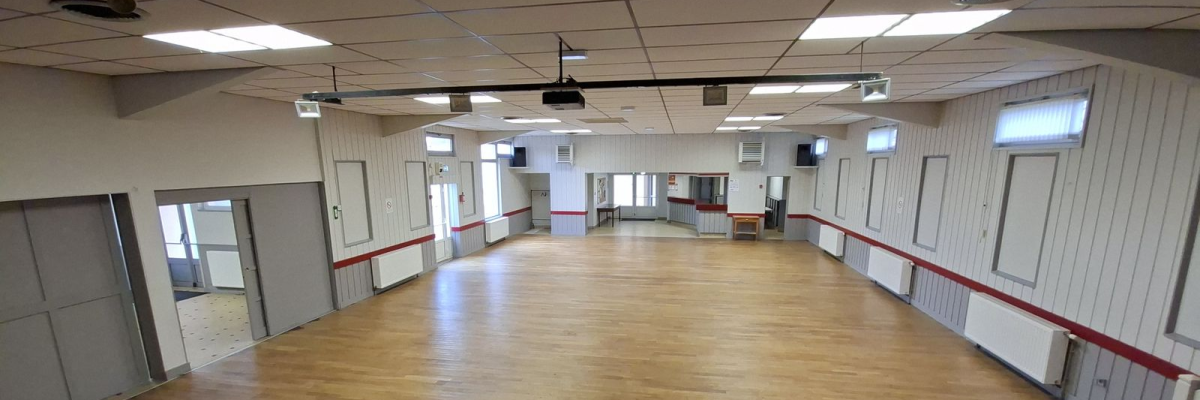 Salle polyvalente avec parquet, lumières, projecteur et portes.