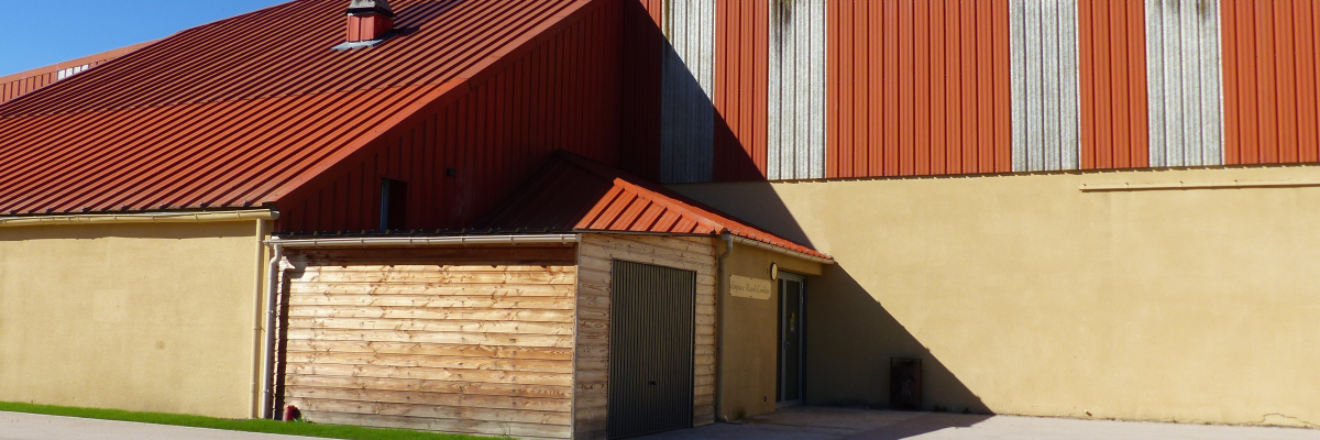 Bâtiment industriel avec toit rouge, murs beiges et orange, porte de garage et cheminée.