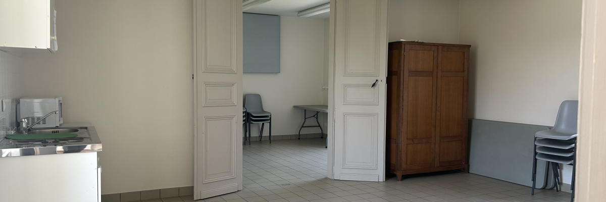 Pièce avec porte, armoire, évier, chaises, table et chariot.