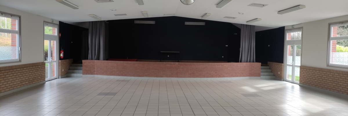 Salle avec scène, projecteurs, rideaux, portes vitrées et éclairage au plafond.