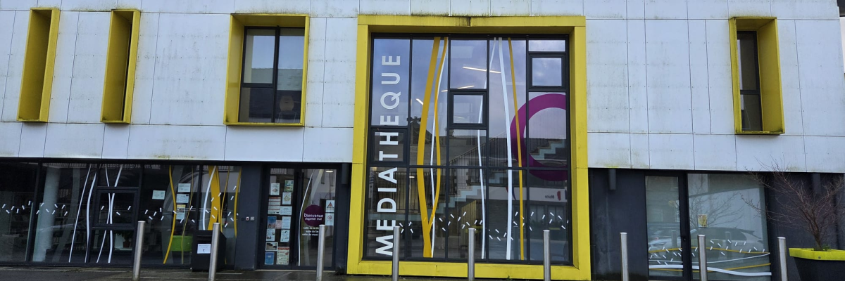 Bâtiment avec façade blanche et jaune, grandes vitres, entrée principale marquée "Médiathèque".