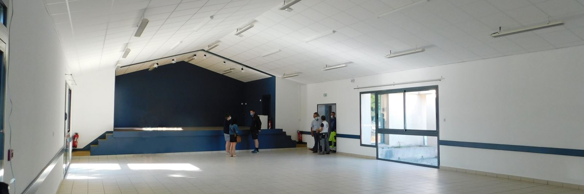Salle spacieuse avec sol carrelé, murs blancs, plafond suspendu, éclairage, porte vitrée et mur bleu.