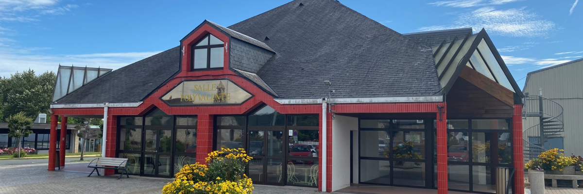 "Bâtiment avec pignons, grandes fenêtres, porte d'entrée, bancs, pots de fleurs, et ciel dégagé."