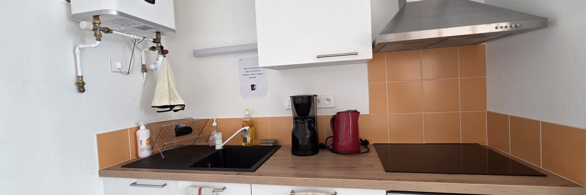 Cuisine avec chauffe-eau, placards, plan de travail, évier, cafetière, hotte, plaques de cuisson et four.