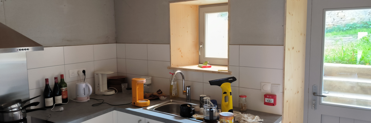 Cuisine avec plan de travail, évier, appareils électroménagers, armoires, porte et fenêtre.